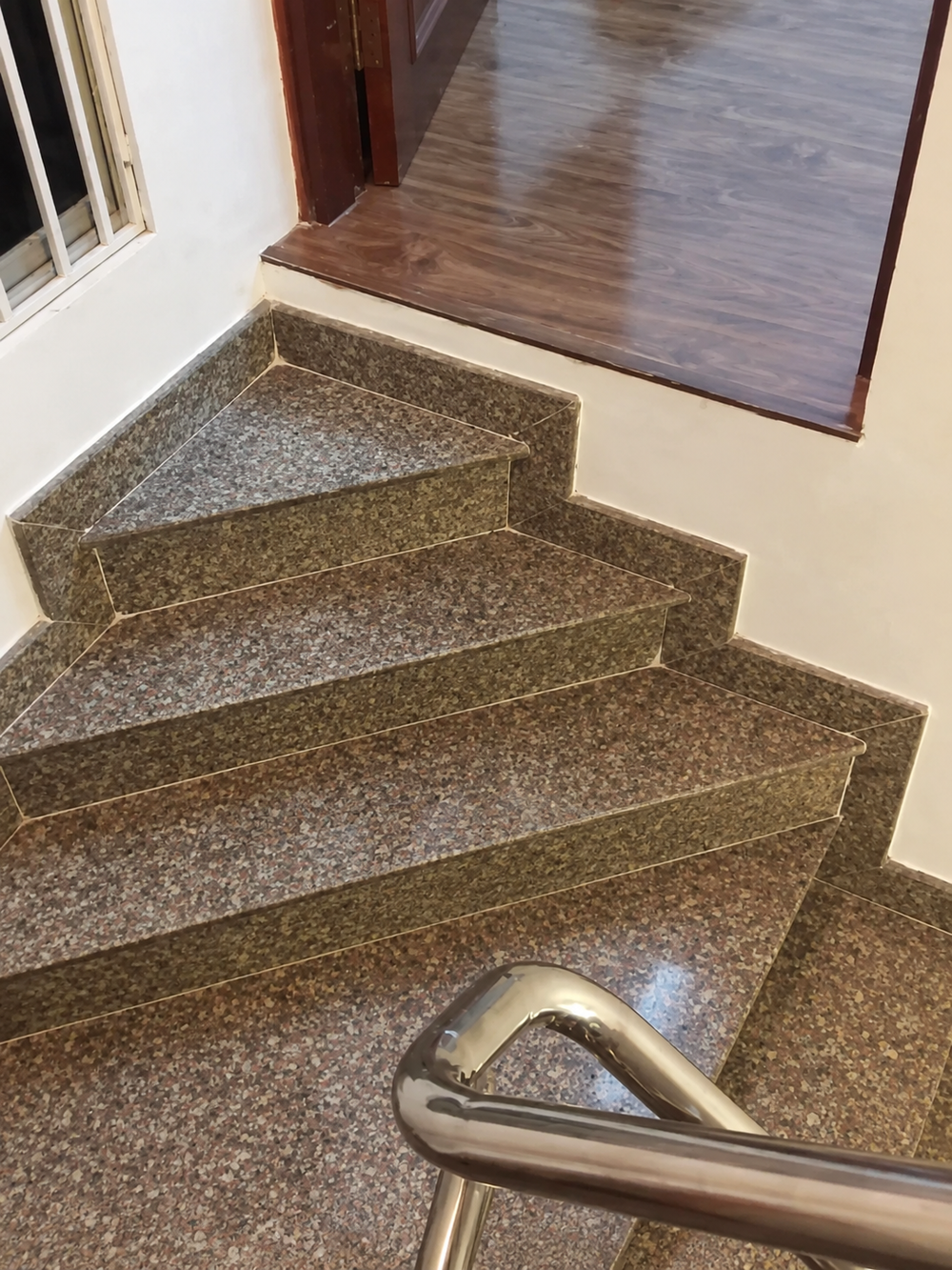 Curved staircase with granite steps and a chrome handrail leading to a wooden floor landing.