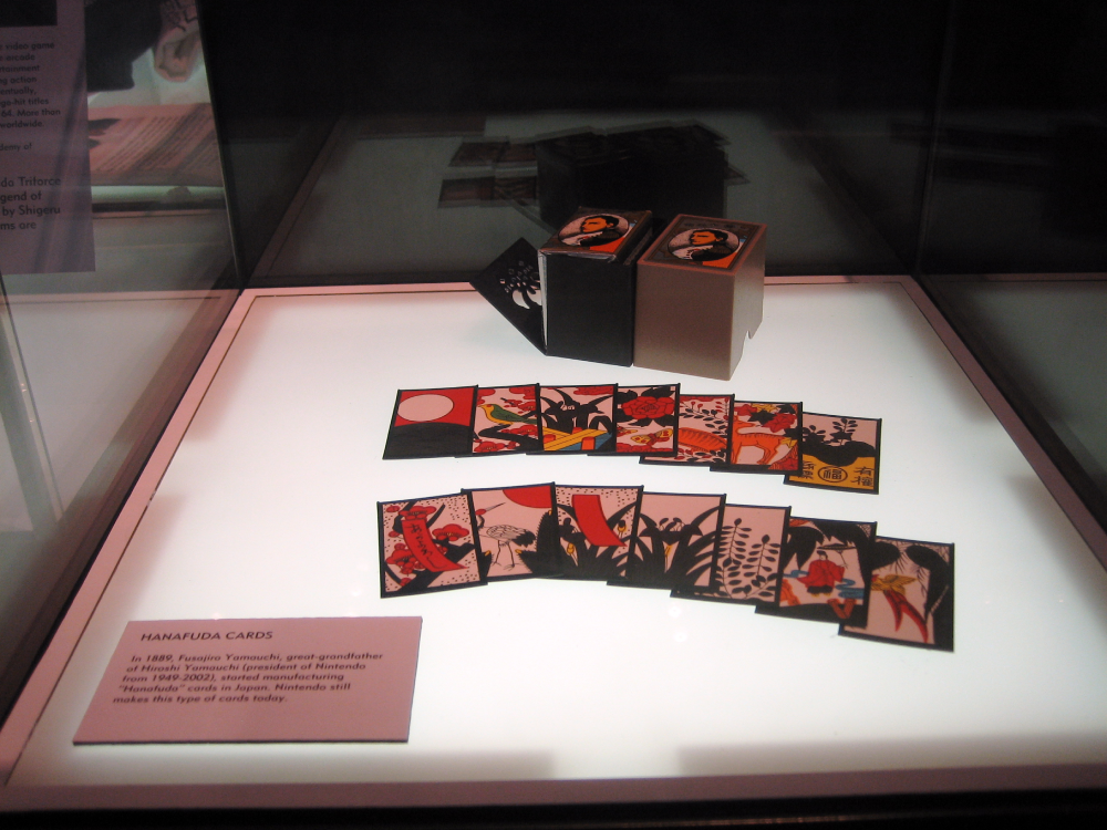 A display of vintage Hanafuda playing cards and their boxes in a glass case, accompanied by a descriptive museum label.