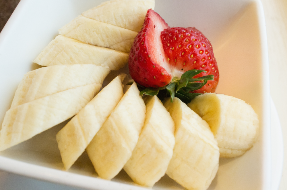 Sliced banana and a whole strawberry in a small white bowl.