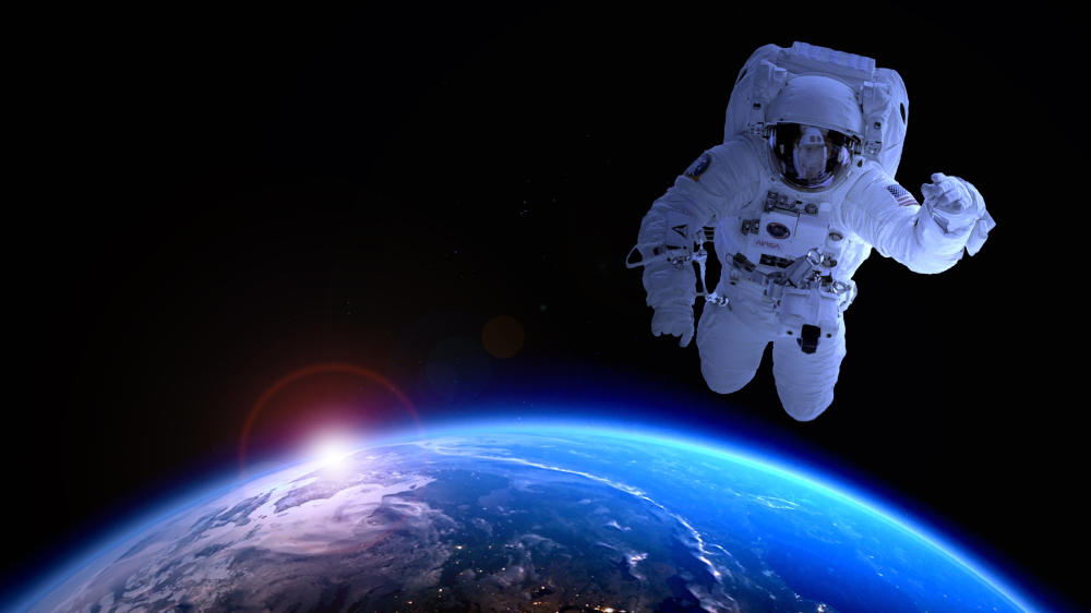An astronaut floats in space above the Earth’s horizon during a sunrise.