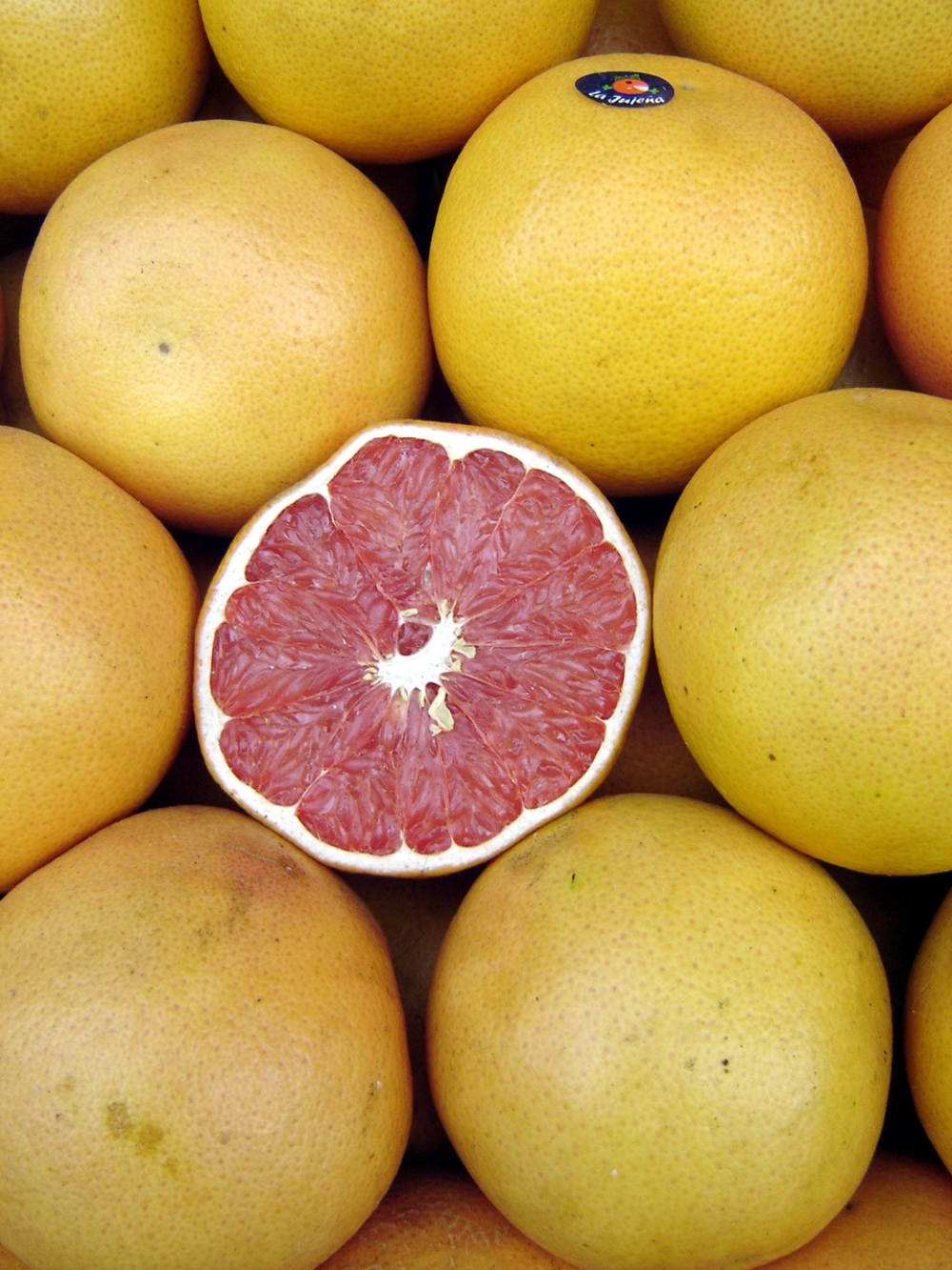A halved ruby red grapefruit surrounded by several whole grapefruits.