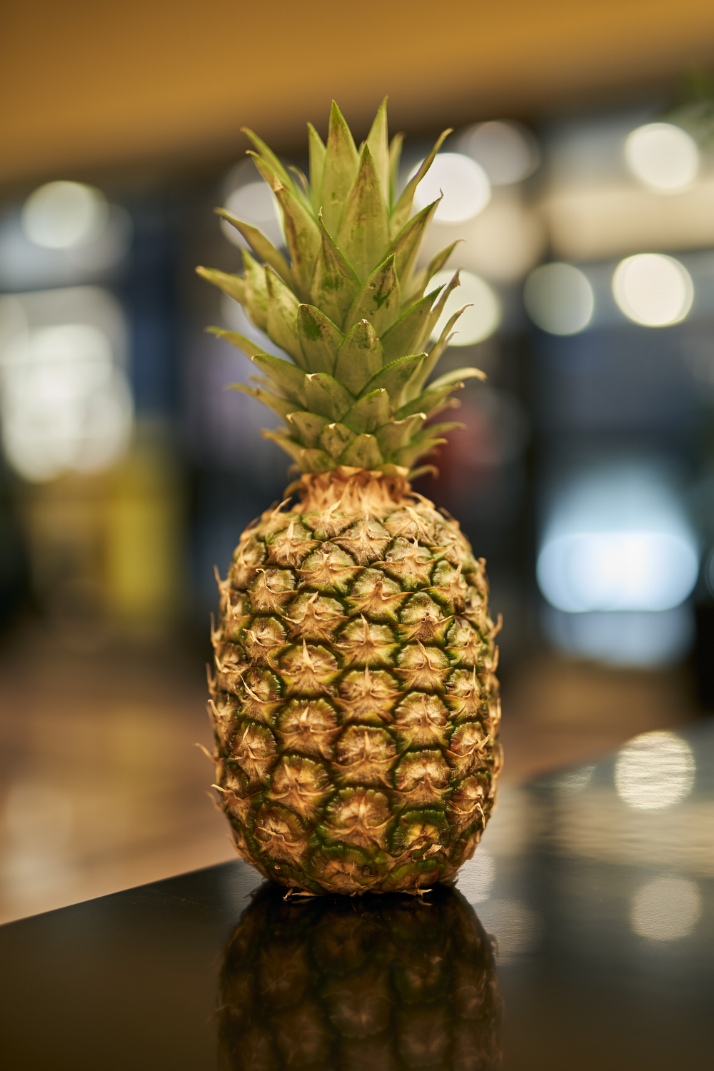 A whole pineapple with green leaves sits on a dark, reflective surface.
