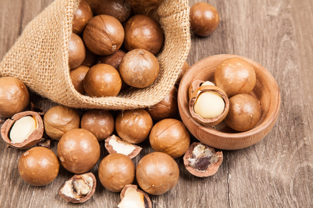 Macadamia nuts in a burlap sack and a small wooden bowl on a wooden surface.