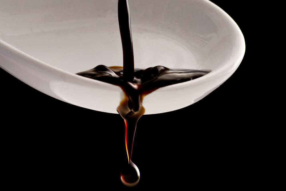Dark liquid pouring into and dripping from a white spoon.