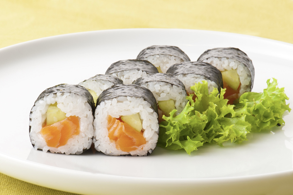 A plate of salmon and cucumber sushi rolls garnished with fresh lettuce.