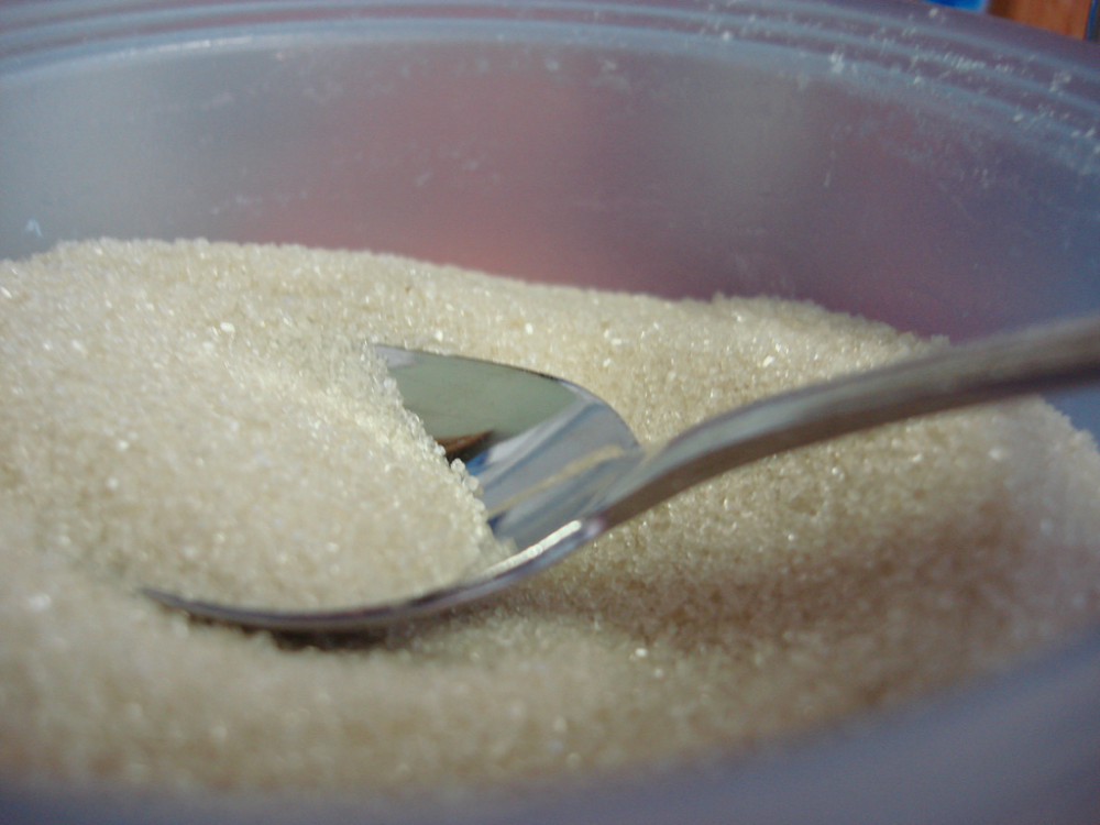 A metal spoon resting in a bowl filled with granulated sugar.