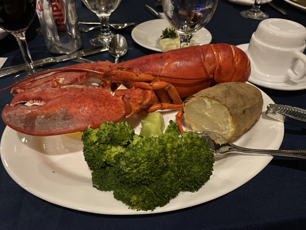 A whole cooked lobster served with a baked potato and steamed broccoli on a white plate.