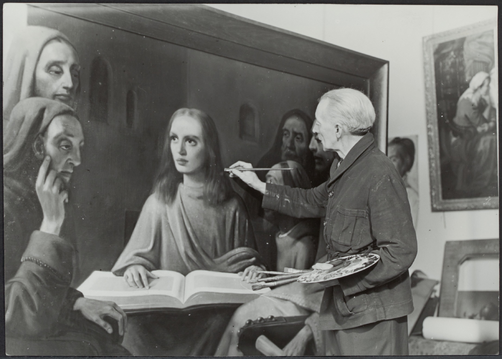 An elderly painter holding a palette and brush works on a large canvas depicting a scene with several figures, including a central youth reading a book.