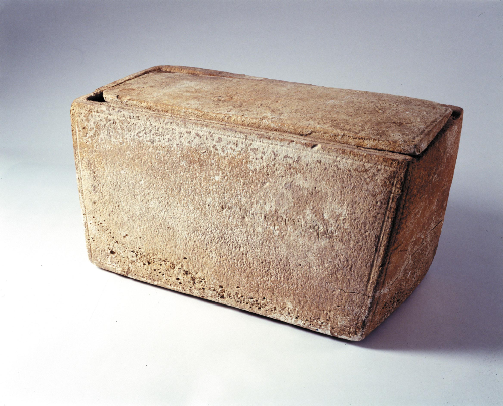 A rectangular stone ossuary with a lid, featuring faint inscribed text on the front side.