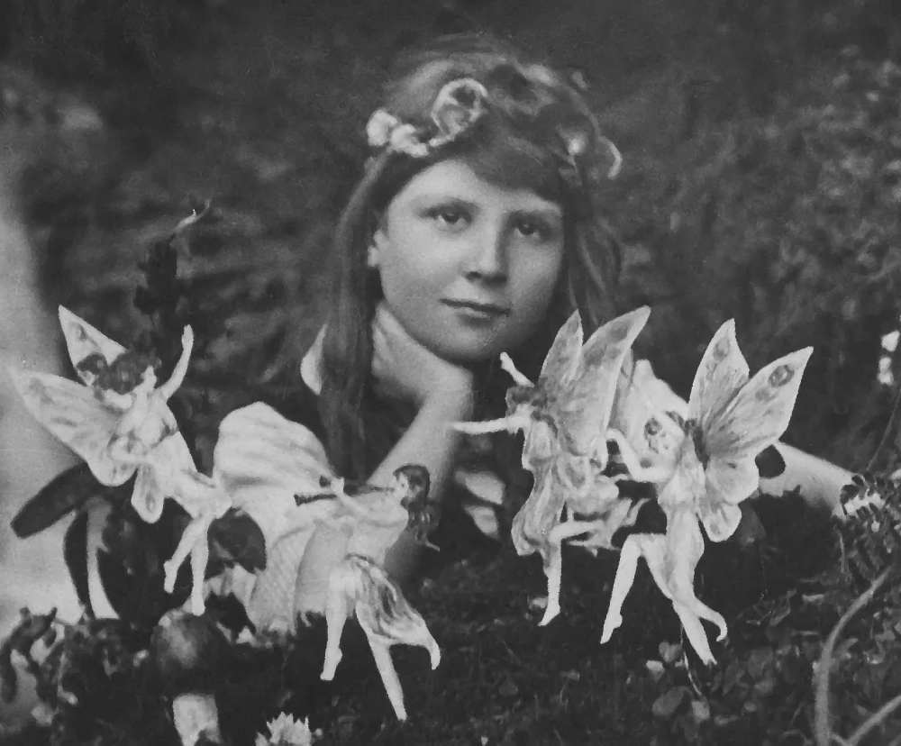 A young girl with a flower crown rests her chin on her hand, surrounded by four small, winged fairies.