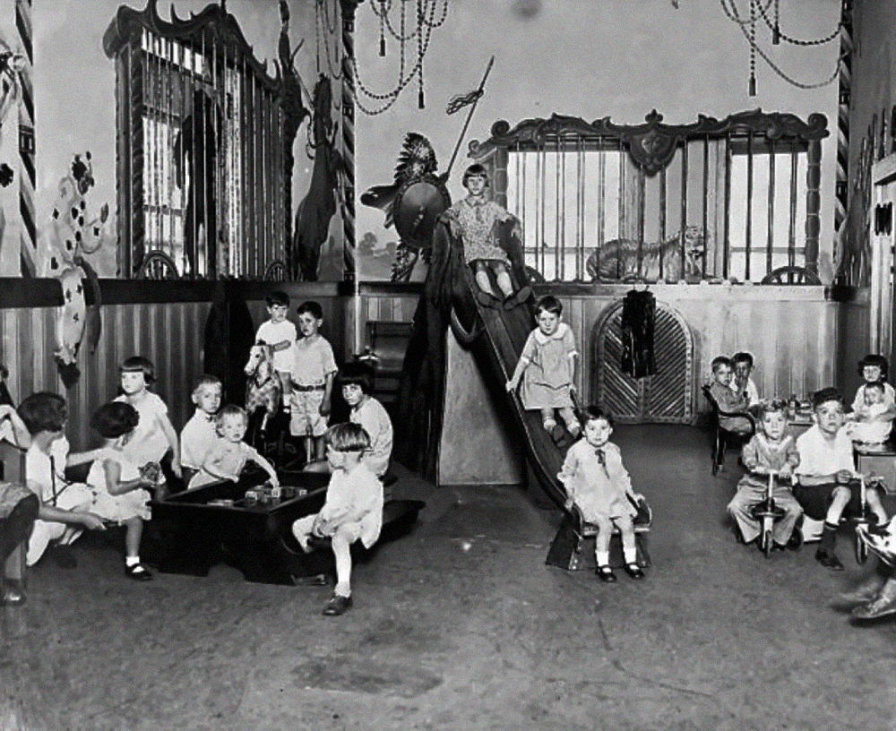 A black-and-white photo of children playing in a nursery decorated with murals of animals in cages.
