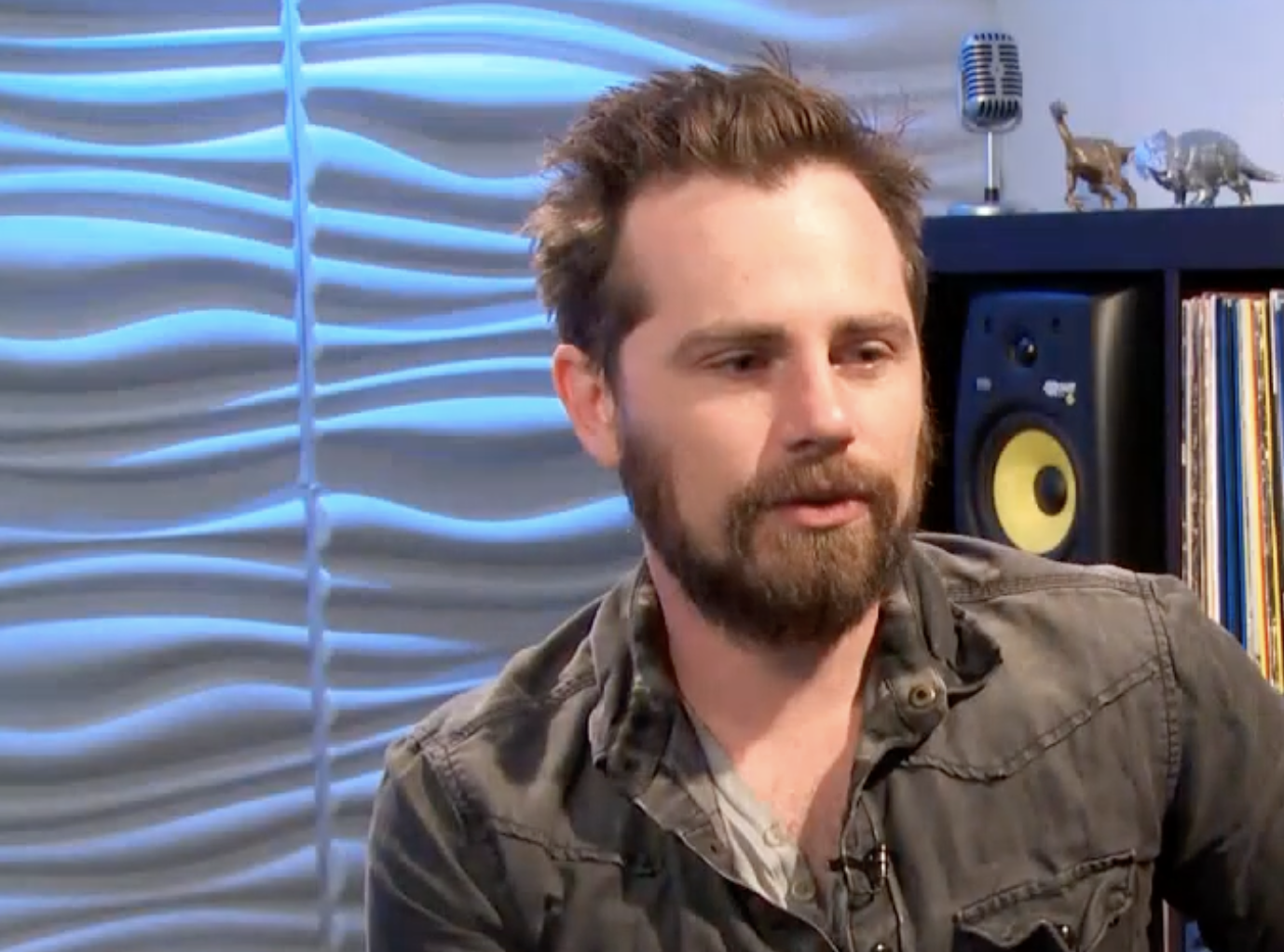 A bearded man with short brown hair speaking into a microphone.