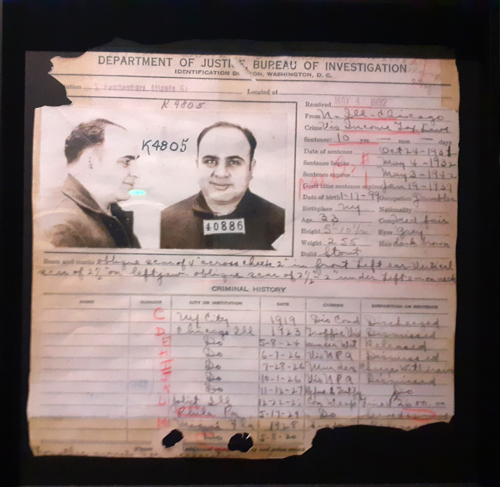 A 1932 FBI identification document for Al Capone featuring two mugshots, his personal physical description, and a hand-written criminal history log.