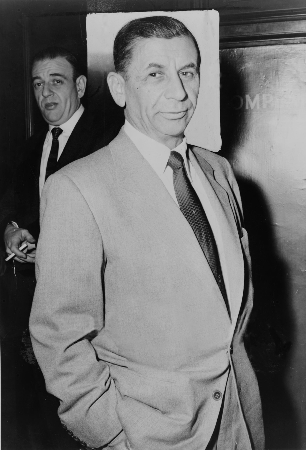 Meyer Lansky in a suit and tie, with a man in a suit and tie standing in the background.