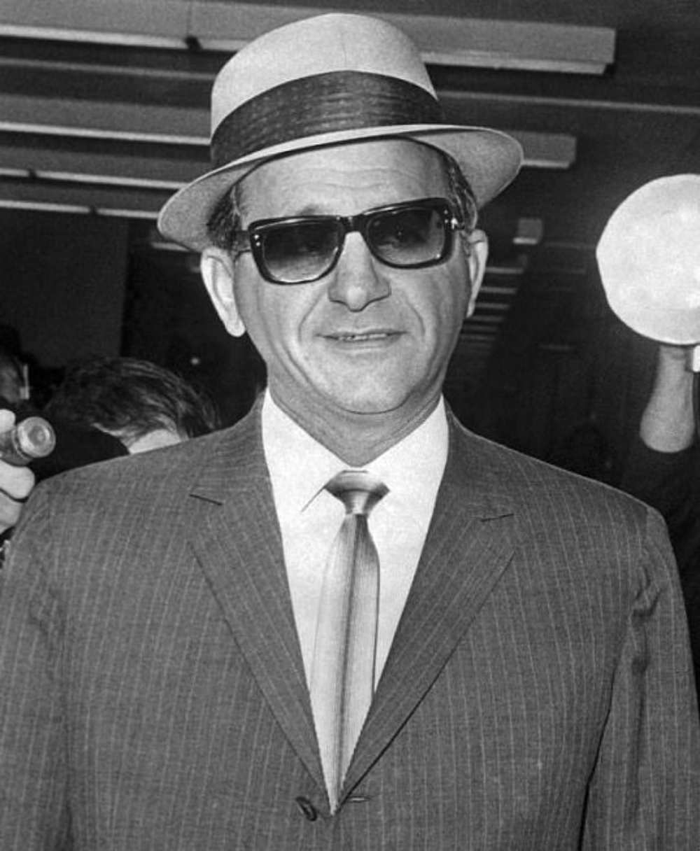 A man in a pinstripe suit, tie, fedora, and sunglasses.