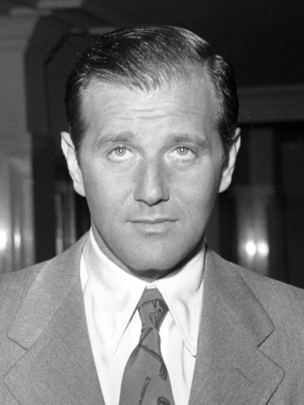 Black and white headshot of a man with short hair wearing a suit and tie.