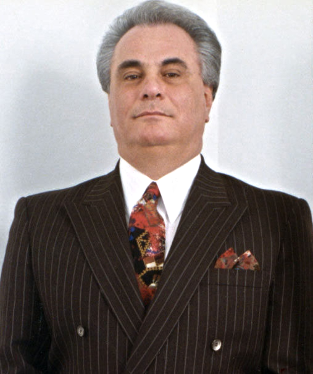 A man with grey hair wearing a pinstriped suit, white shirt, and patterned tie.