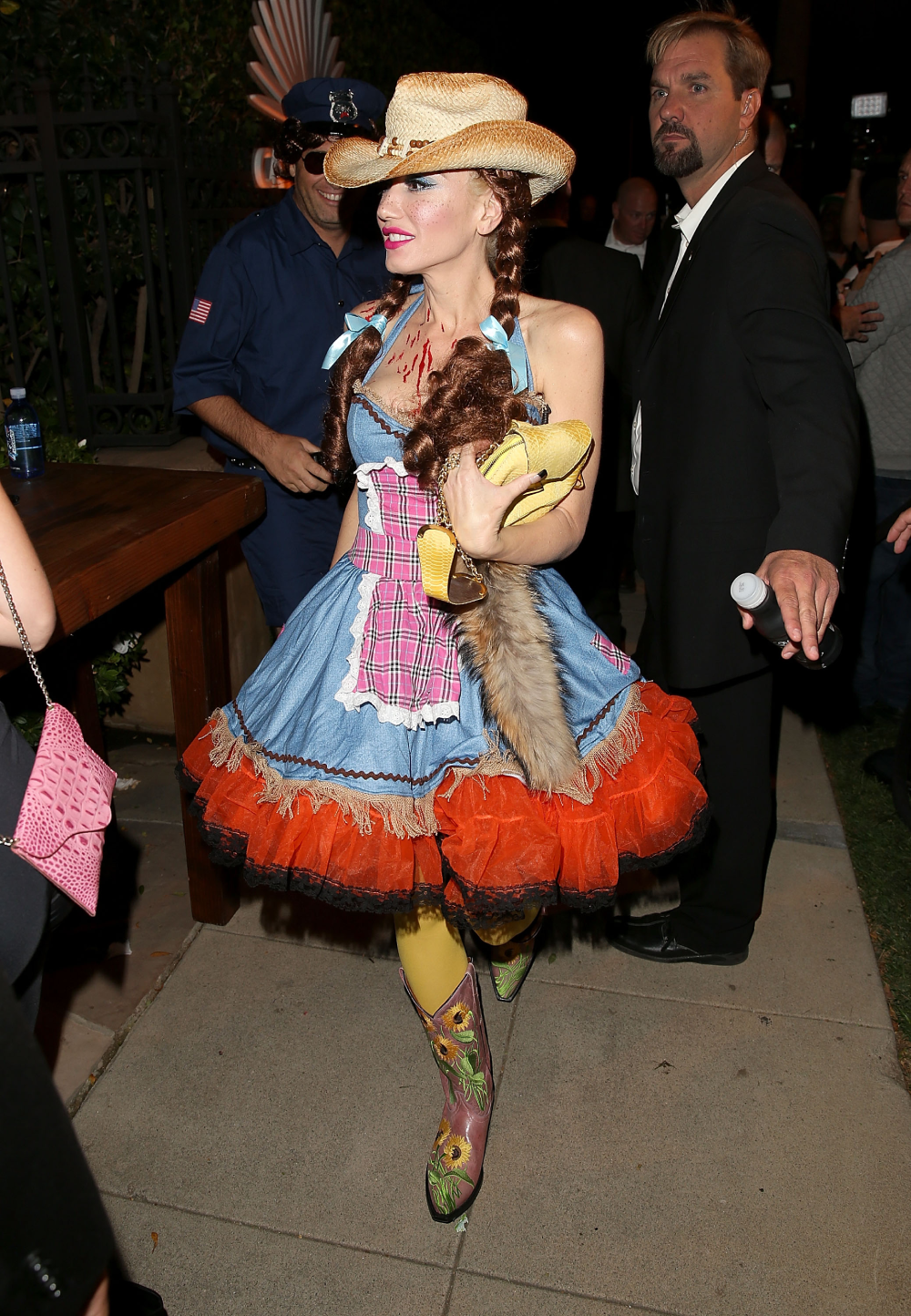 Gwen Stefani wearing a cowgirl costume with a straw hat, denim dress, and sunflower-patterned boots.