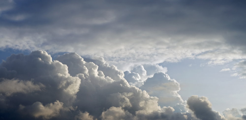 Large, fluffy clouds fill the sky, with some areas brightly lit by sunlight and patches of blue sky visible in the background.