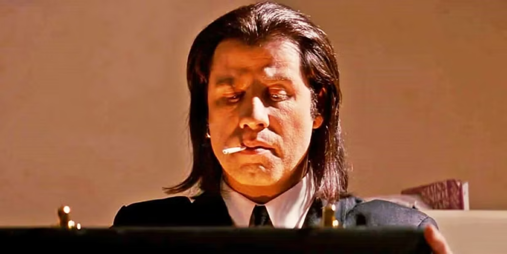 John Travolta as Vincent Vega with a cigarette in his mouth, looking down at an open briefcase.