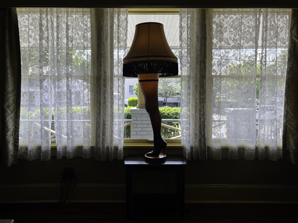 The iconic leg lamp from A Christmas Story sitting on a small table in front of a window with lace curtains.