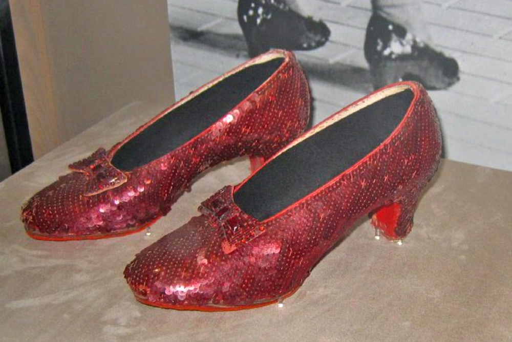 A pair of red sequined pumps with low heels displayed on a pedestal.