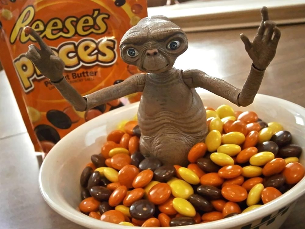 An E.T. the Extra-Terrestrial action figure sitting in a bowl of Reese’s Pieces with a bag of the candy in the background.