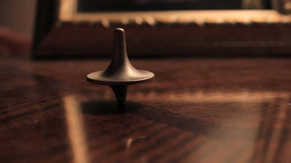 A metal spinning top rotates on a wooden table.