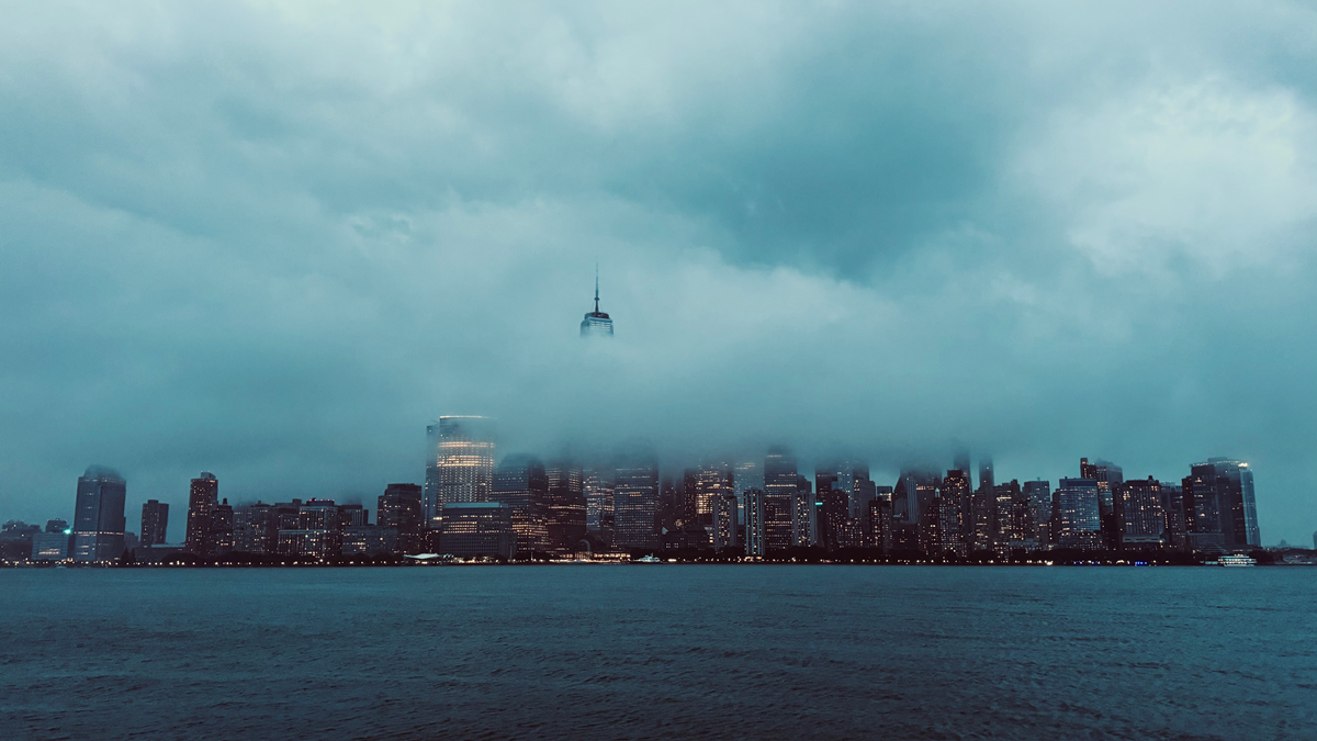 The New York City skyline partially obscured by a thick layer of low-hanging clouds over the water.