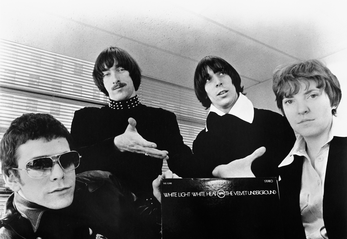 The band The Velvet Underground poses together, with one member holding their album White Light/White Heat.
