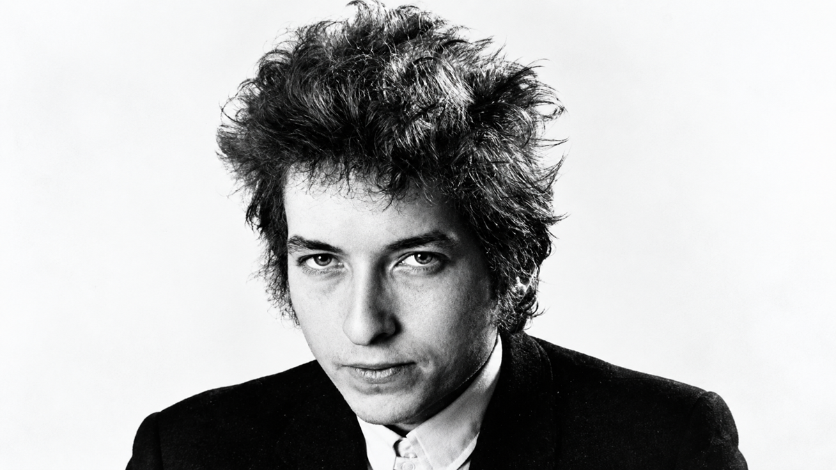 A black and white portrait of a young Bob Dylan looking directly at the camera.