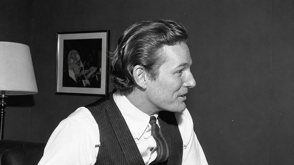 Profile view of a man in a dress shirt, striped tie, and vest.