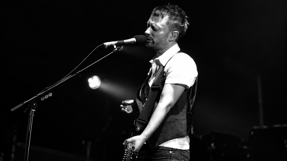 A musician playing a guitar and singing into a microphone on stage.