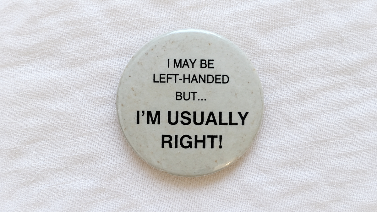 A round pinback button that reads “I MAY BE LEFT-HANDED BUT... I’M USUALLY RIGHT!”