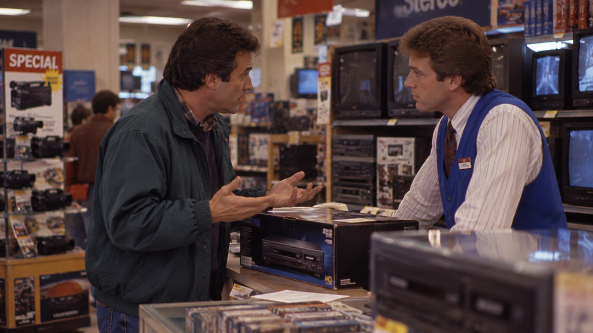 A customer talking to a store clerk behind a counter in an electronics store.