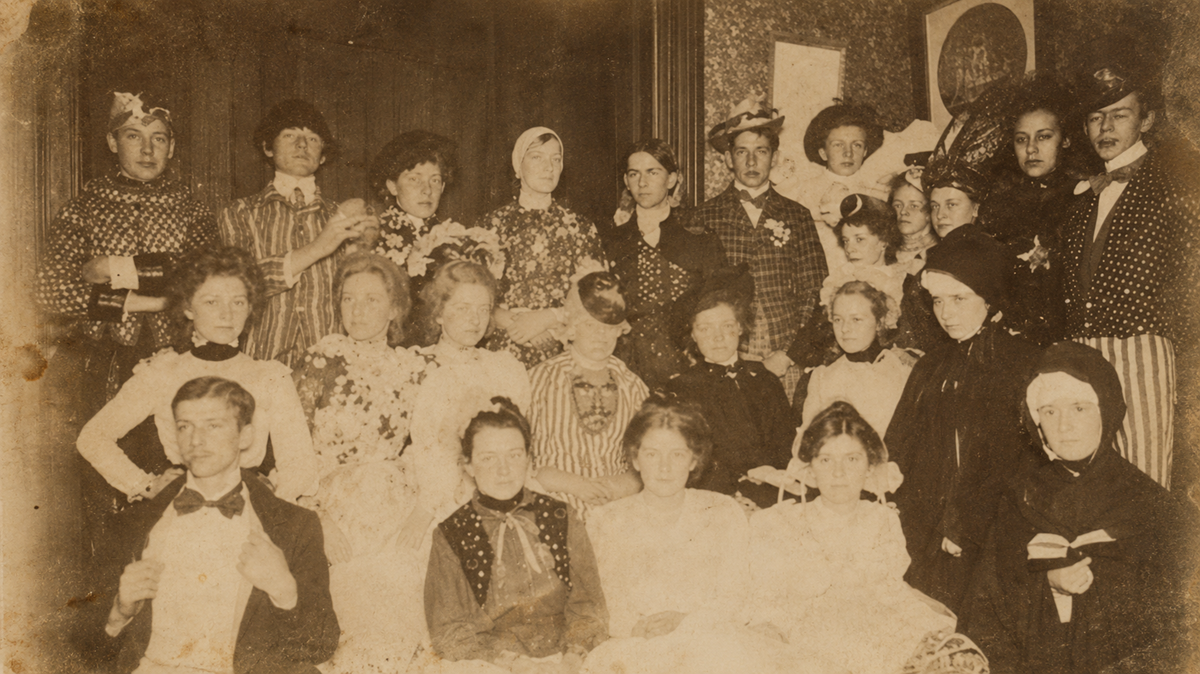 A large group of men and women in late 19th-century formal attire posed for a vintage studio portrait.