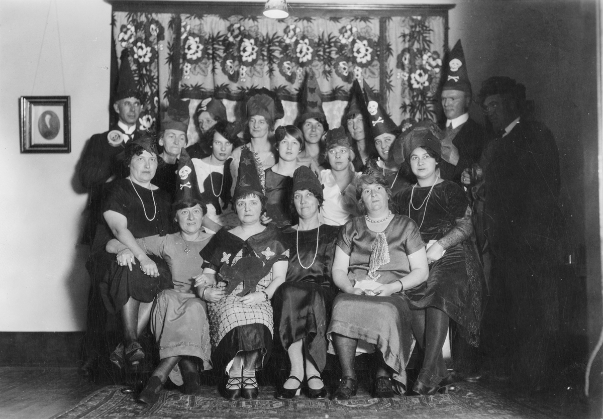 A group of men and women posing for a formal portrait while wearing party hats, some decorated with skull and crossbones.