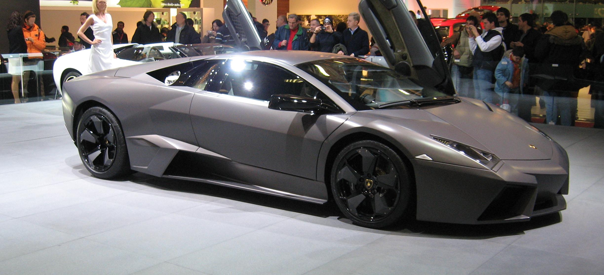A matte grey Lamborghini Reventón sports car with its scissor door open on display at a trade show.
