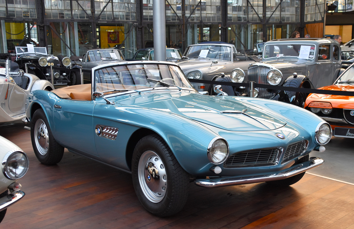 A vintage blue BMW 507 convertible parked in a car museum among other classic vehicles.