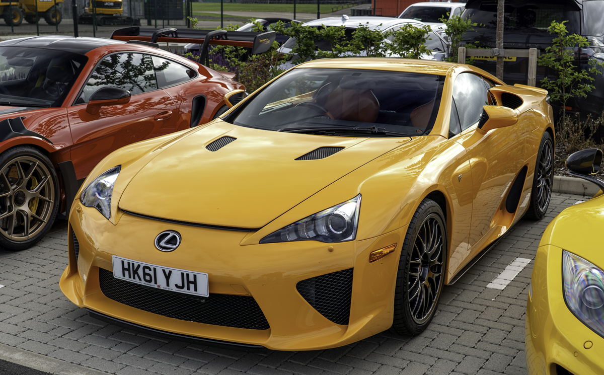 Yellow Lexus LFA parked in a lot next to an orange sports car.