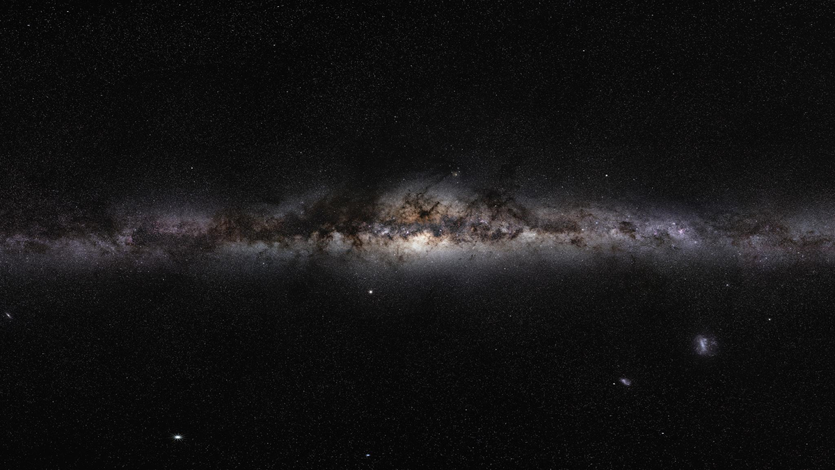 A panoramic view of the Milky Way galaxy stretching across a vast, dark star-filled sky.
