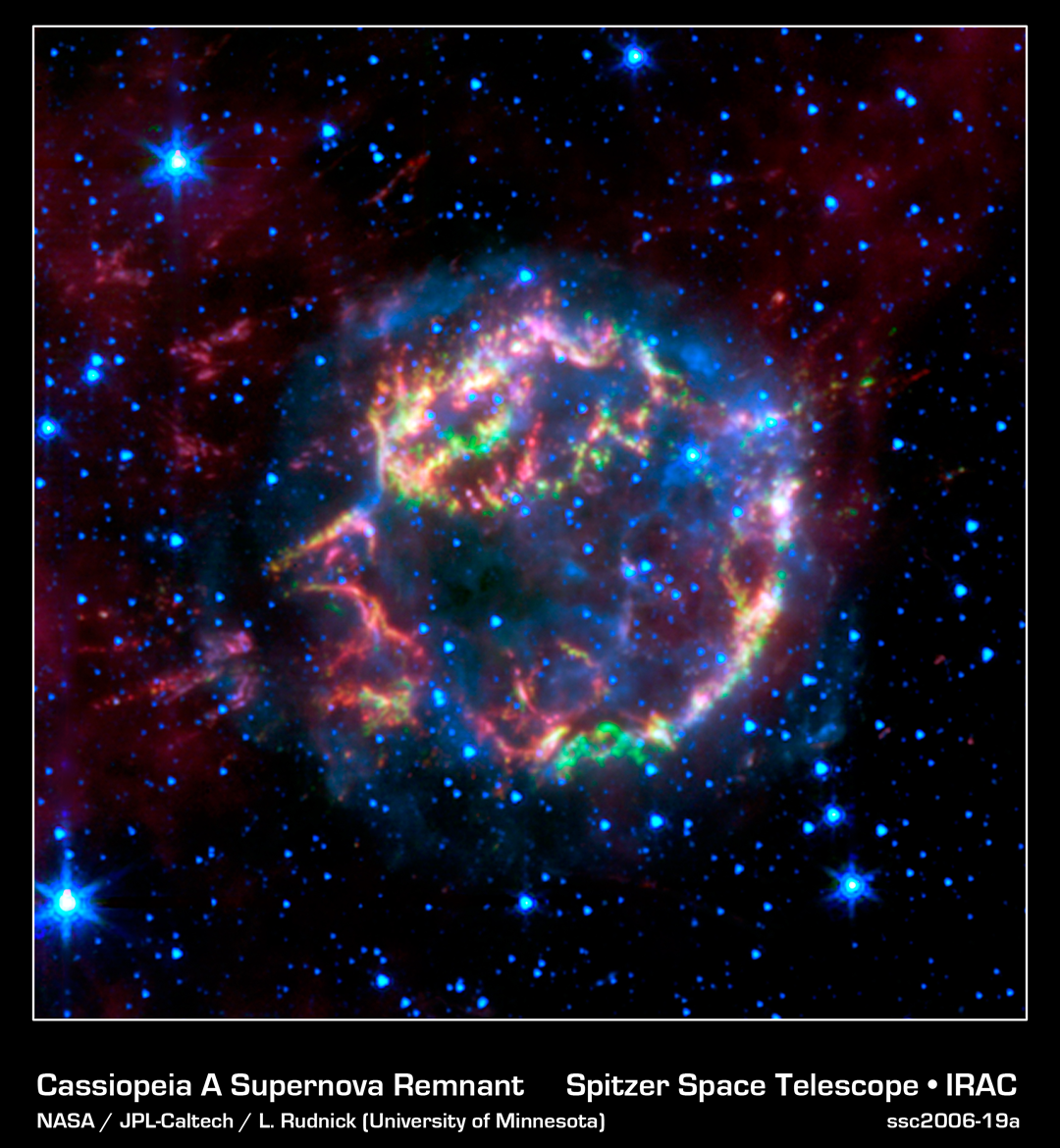 The Cassiopeia A supernova remnant glows with vibrant colors of red, green, and blue against a dark field of stars.