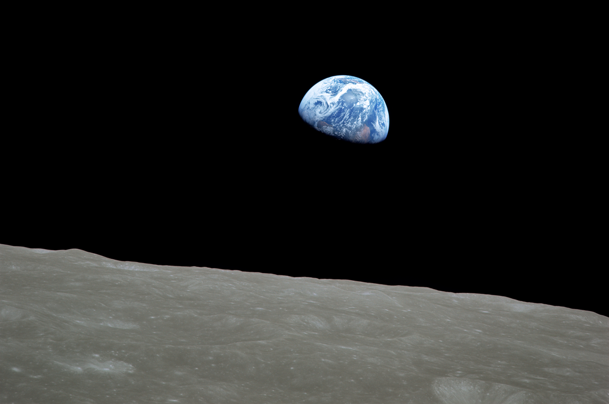 The Earth rising above the barren, cratered horizon of the Moon against the blackness of space.