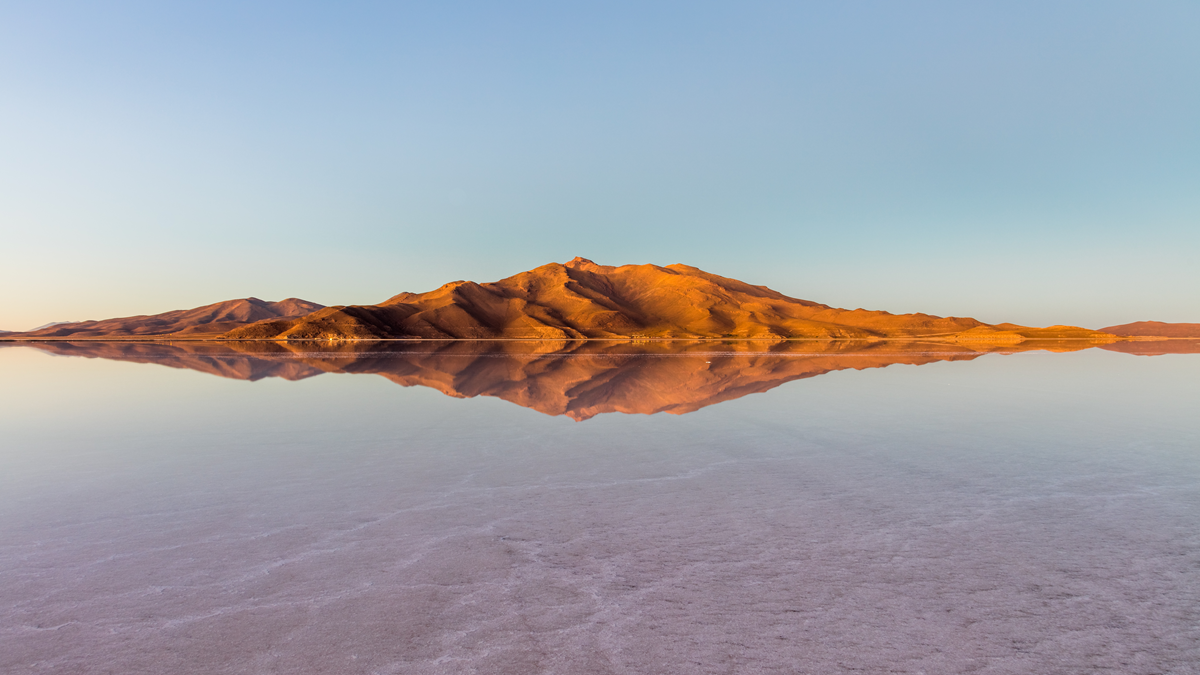 A golden mountain range reflected perfectly in the still water of a salt flat.