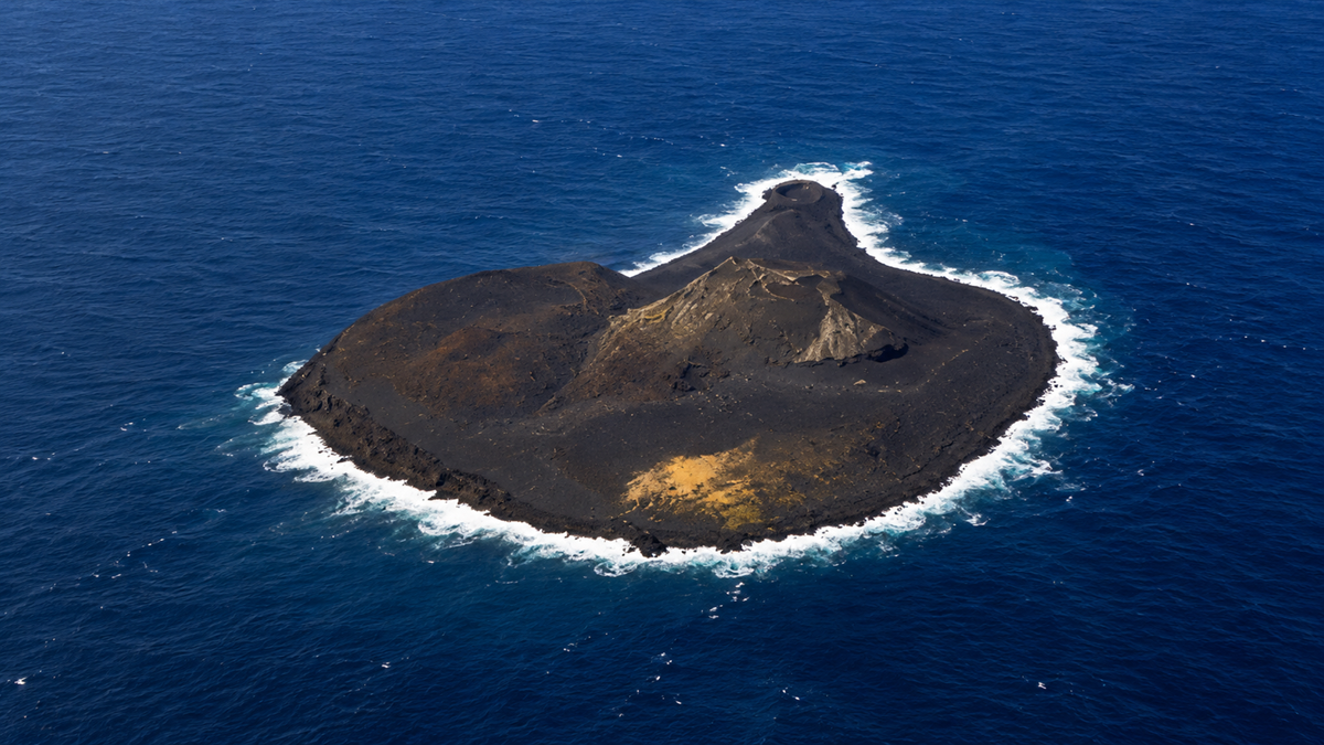 Aerial view of a volcanic island surrounded by deep blue ocean water.
