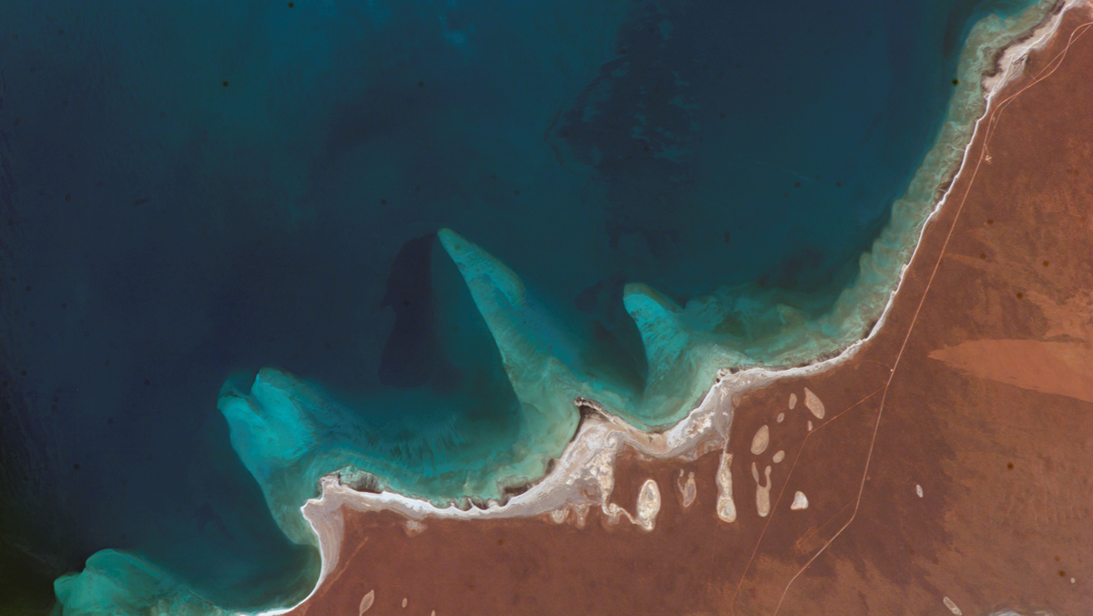 Aerial view of a jagged coastline where dark blue ocean water meets reddish-brown land.