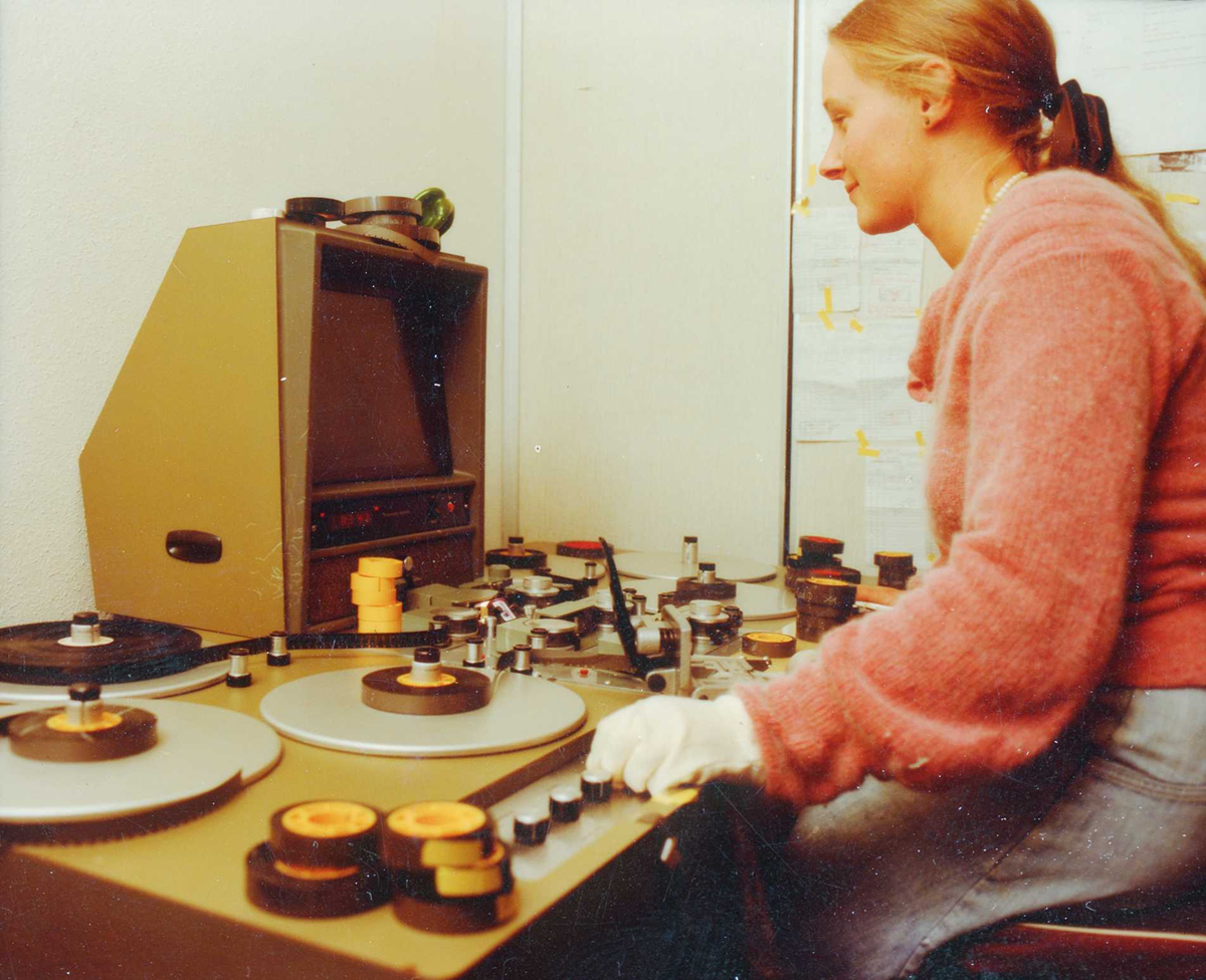 A woman wearing white gloves edits film on a flatbed editing machine.