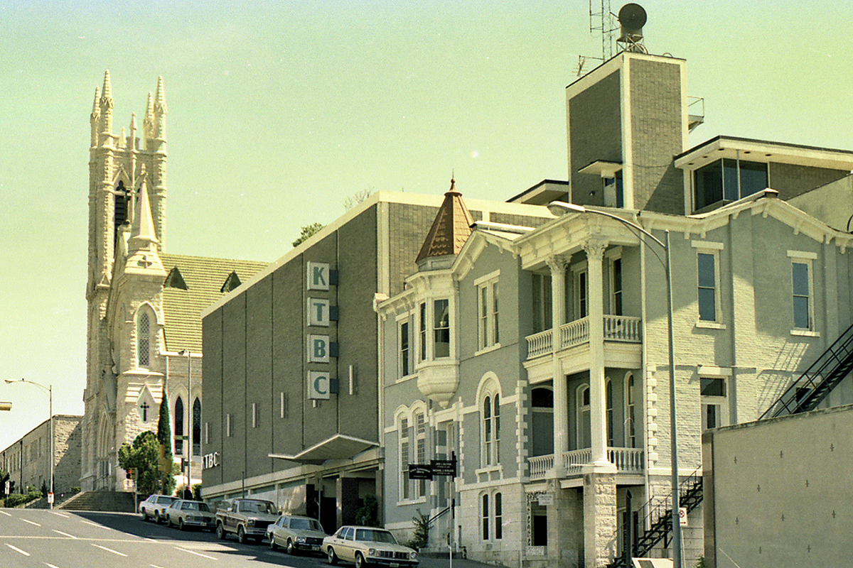 A street view of the KTBC building next to a historic church, with cars parked along the curb.