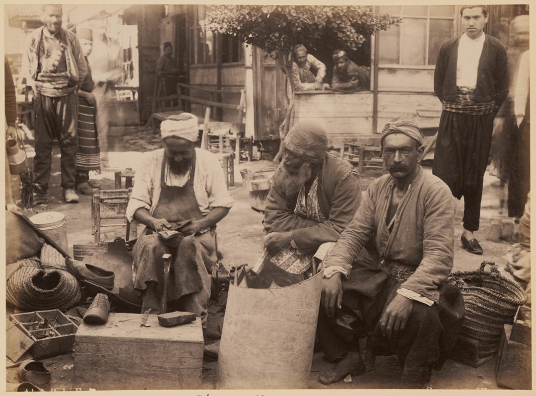 Three men sit in a courtyard while working on leather, surrounded by other people and various tools and baskets.