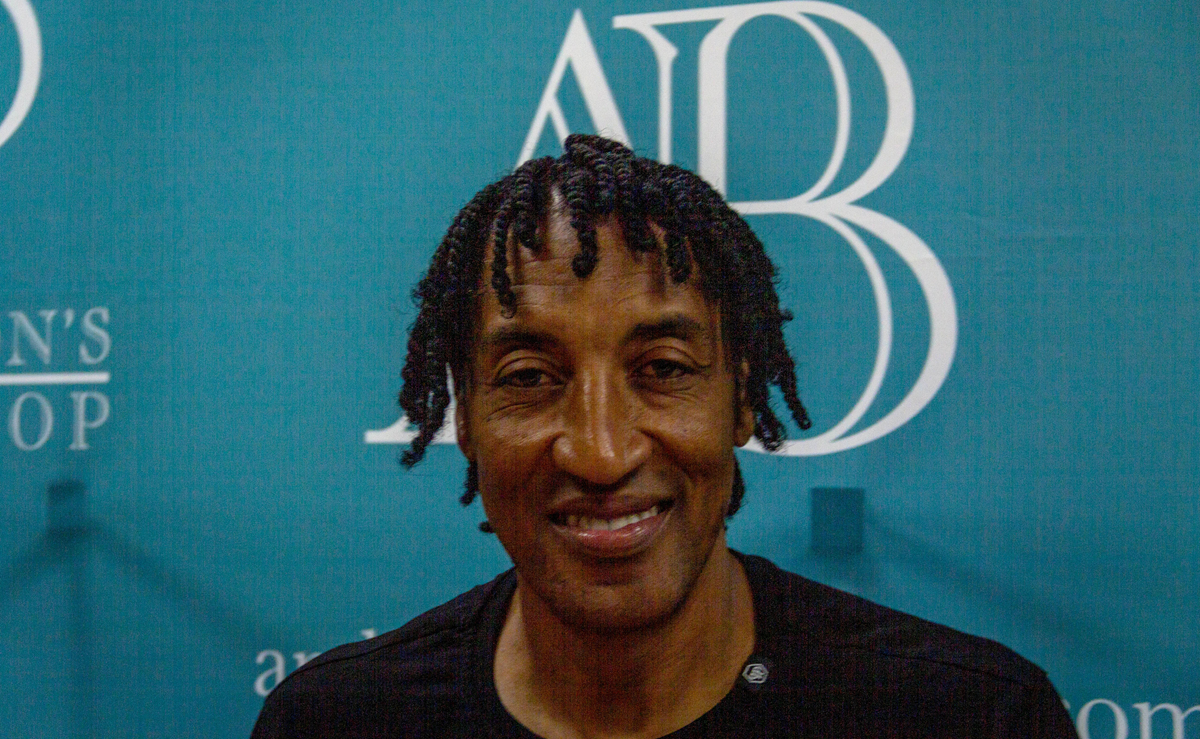 Scottie Pippen smiling in front of a branded teal backdrop.